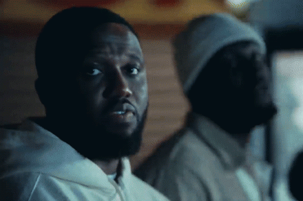 Headie One in a white hoodie looks directly forward, with Stormzy wearing a beanie in the dark background