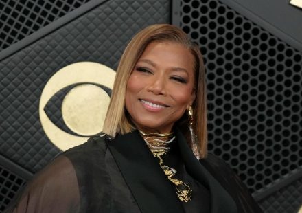 Queen Latifah smiling with a sleek blonde bob hairstyle and gold necklace against a dark backdrop