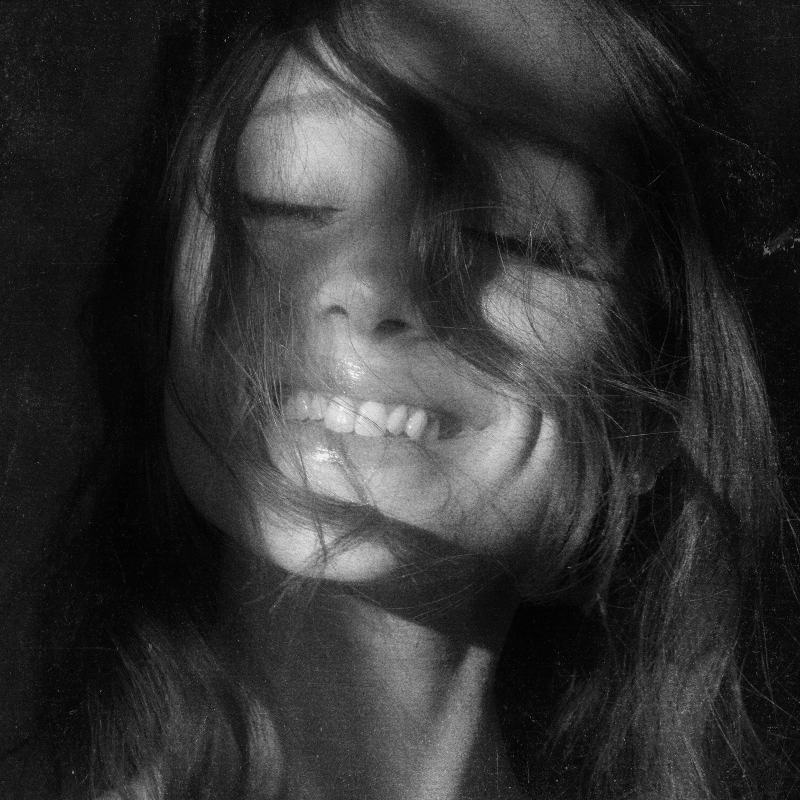 Close-up black and white portrait of a Ariana Grande smiling with eyes closed and hair blowing across her face
