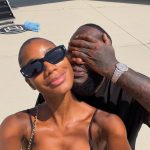 Rick Ross covering his eyes while posing for a selfie with a woman on an airport tarmac