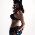 Woman in a black bra, jeans, and captain's hat with "RB" in pearls, looking over her shoulder