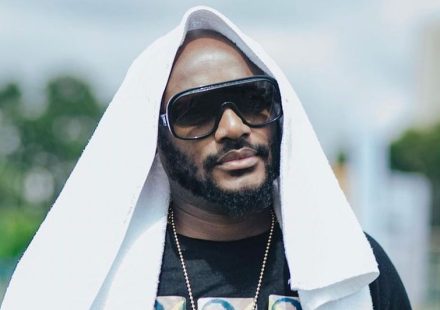 2Baba with a beard wearing large dark sunglasses, a gold chain, and a white towel draped over his head