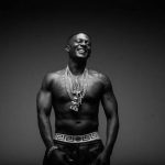 Boosie Badazz smiling and shirtless while wearing several heavy chains in a black and white portrait