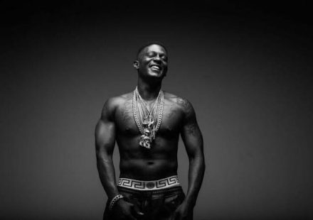 Boosie Badazz smiling and shirtless while wearing several heavy chains in a black and white portrait