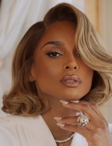 Ciara with styled blonde hair and glamorous makeup, showcasing a large diamond ring