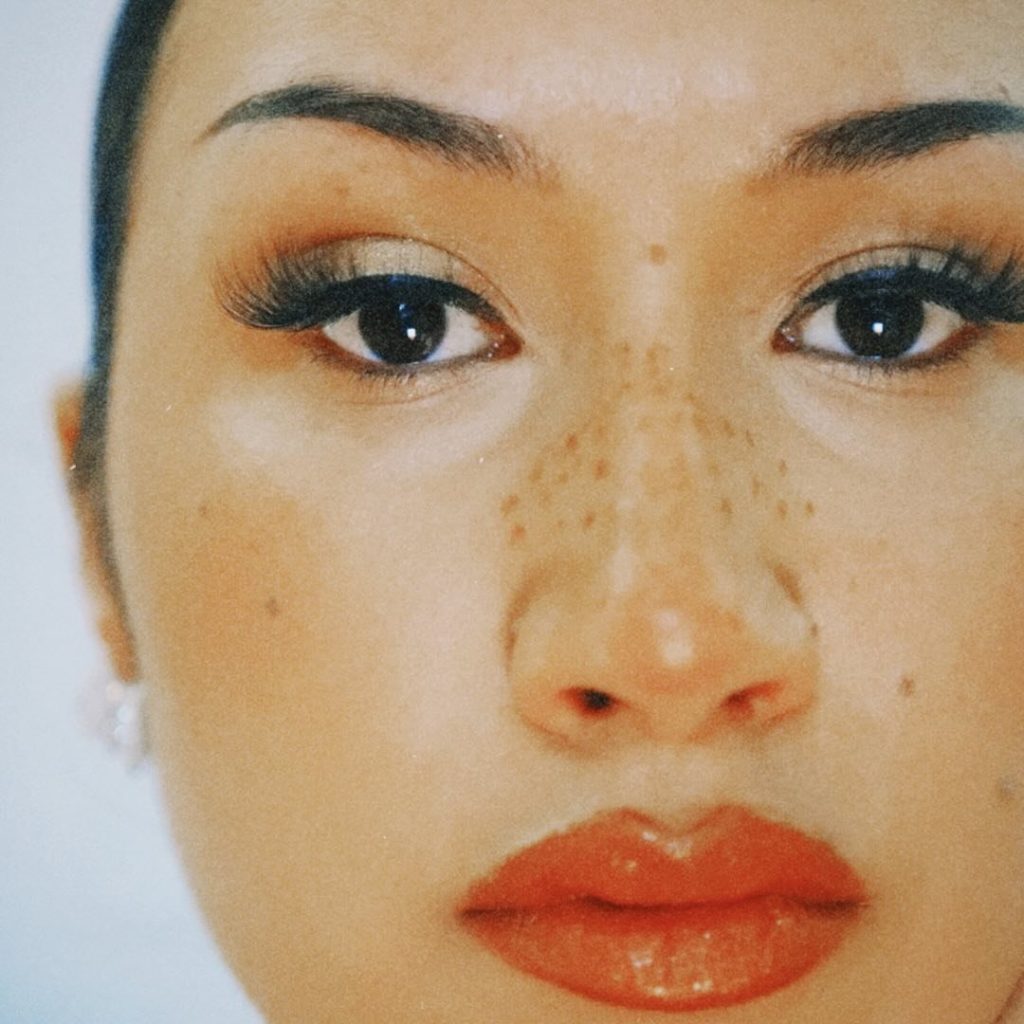 Close-up of a Cleo Sol's face with freckles across their nose, long eyelashes, and red lipstick