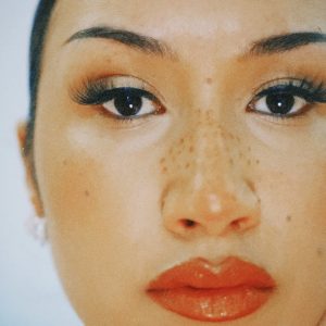 Close-up of a Cleo Sol's face with freckles across their nose, long eyelashes, and red lipstick