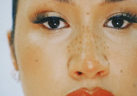 Close-up of a Cleo Sol's face with freckles across their nose, long eyelashes, and red lipstick