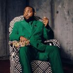 Davido sitting in a patterned chair wearing a green suit and holding a gold crown