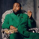 Davido sitting in a patterned chair wearing a green suit and holding a gold crown