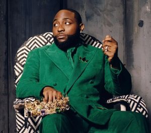 Davido sitting in a patterned chair wearing a green suit and holding a gold crown