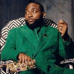 Davido sitting in a patterned chair wearing a green suit and holding a gold crown