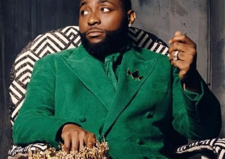 Davido sitting in a patterned chair wearing a green suit and holding a gold crown
