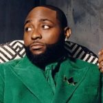 Davido sitting in a patterned chair wearing a green suit and holding a gold crown