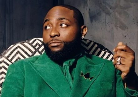 Davido sitting in a patterned chair wearing a green suit and holding a gold crown