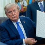 Donald Trump sitting at a desk and holding up a signed document