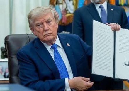 Donald Trump sitting at a desk and holding up a signed document