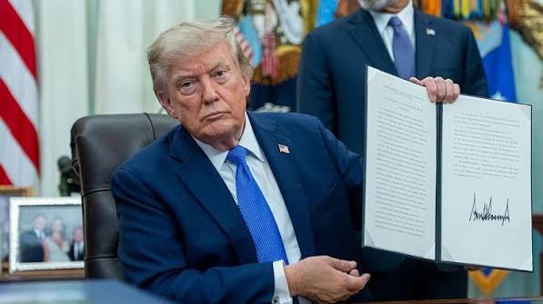 Donald Trump sitting at a desk and holding up a signed document