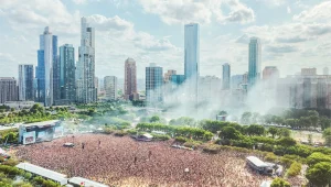 Aerial view of a massive crowd at a music festival in a city park with a backdrop of skyscrapers