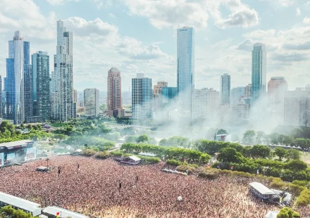 Aerial view of a massive crowd at a music festival in a city park with a backdrop of skyscrapers