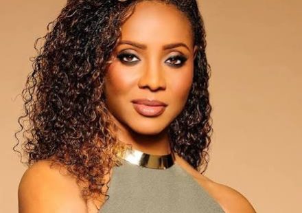 MC Lyte with curly, highlighted brown hair wearing smoky eye makeup and a gold choker necklace