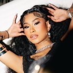 Ming Luanli with long curly hair and full makeup lying down, wearing a thick chain necklace and silver bracelets