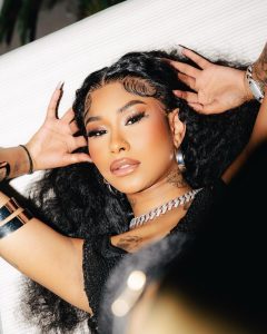 Ming Luanli with long curly hair and full makeup lying down, wearing a thick chain necklace and silver bracelets