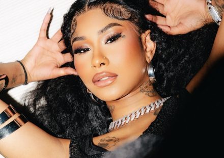 Ming Luanli with long curly hair and full makeup lying down, wearing a thick chain necklace and silver bracelets