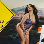 Rihanna poses in a blue floral bodysuit in a desert next to a yellow sign that says Curves Ahead