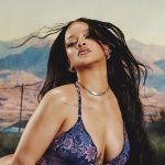 Rihanna poses in a blue floral bodysuit in a desert next to a yellow sign that says Curves Ahead