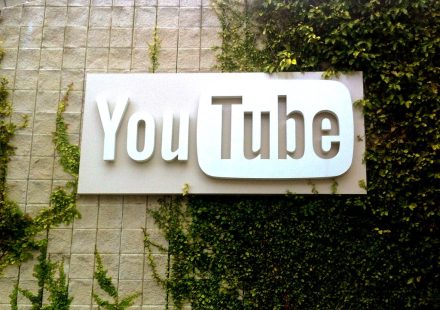 Large white YouTube logo sign mounted on a stone wall partially covered with green ivy