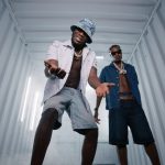 J Hus and Marnz Malone posing inside a lighted metal shipping container wearing unbuttoned shirts and chains