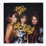 The Keen sisters posing together at night, with the center woman holding bright bouquets of sunflowers