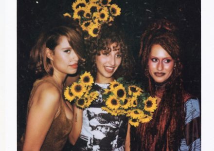 The Keen sisters posing together at night, with the center woman holding bright bouquets of sunflowers