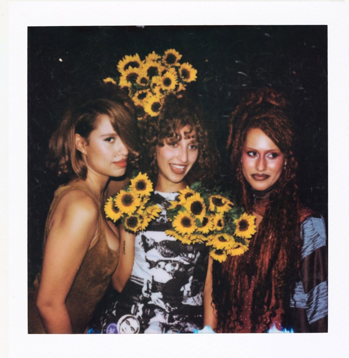 The Keen sisters posing together at night, with the center woman holding bright bouquets of sunflowers